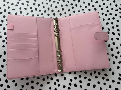 Pink planner with a metal ring binder on a polka dot background