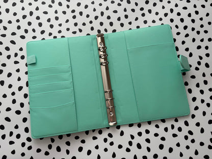 Turquoise planner with a metal binder clip on a polka dot background
