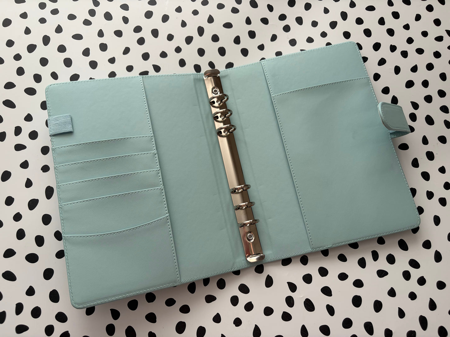 Light blue leather planner with a metal ring on a polka dot background